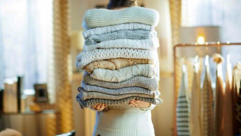 Woman holding a stack of folded winter sweaters.