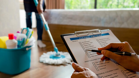 Person checking off a cleaning checklist while another person mops.