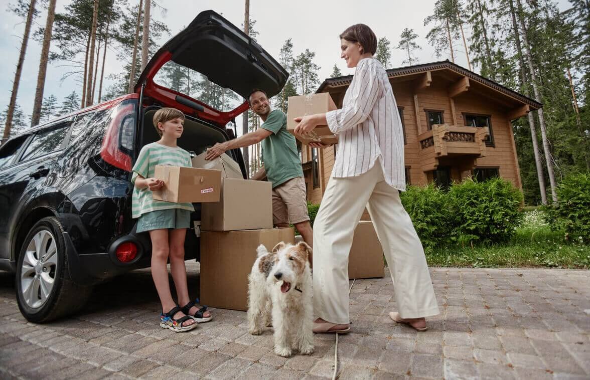 Family loading boxes into the trunk of their car with their dog at their feet