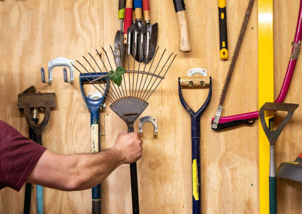 Man hangs gardening tools up on hooks in storage