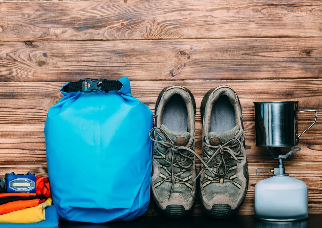 Tent, headlamp, boots, and other camping gear sitting on a wooden table.