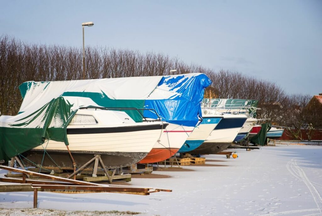 A group of boats in a line in the parking lot for storage over winter.