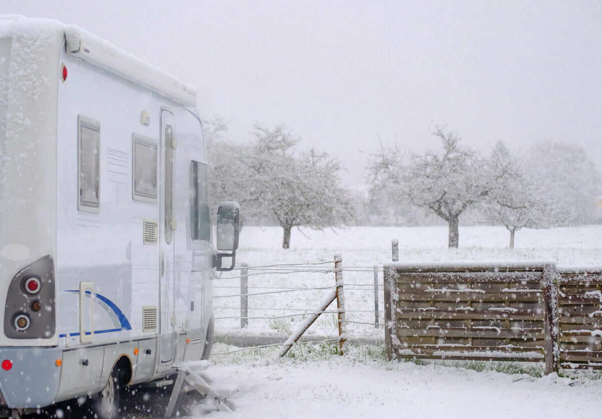 A recreational vehicle parked in storage near fencing on a snowy day.