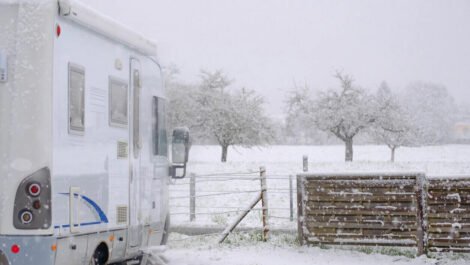 A recreational vehicle parked in storage near fencing on a snowy day.