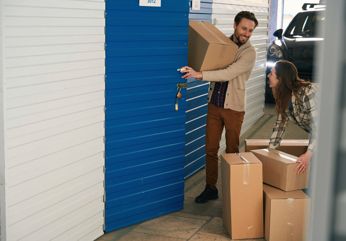 Couple smiles while moving boxes into a storage unit.