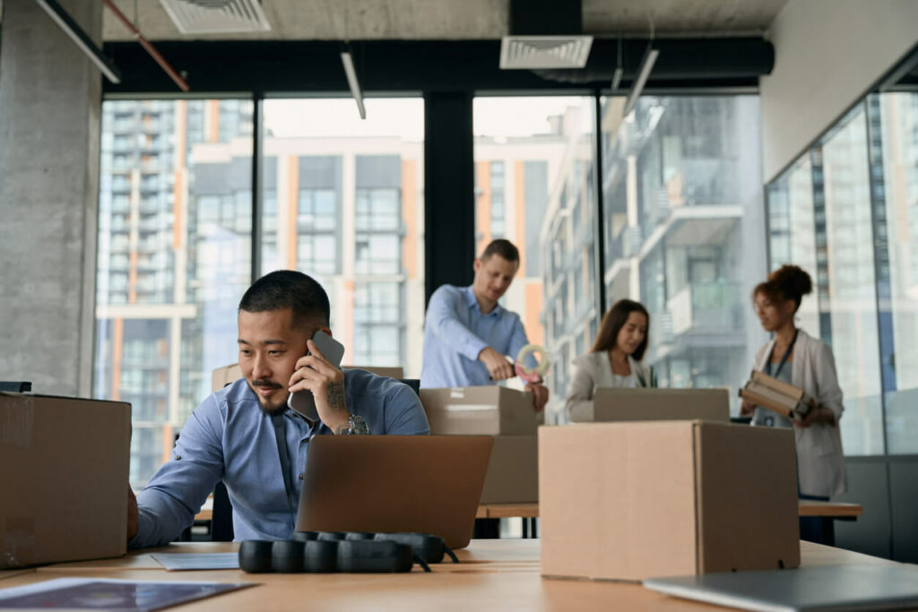 Office workers pack up boxes while the manager talks on his telephone.