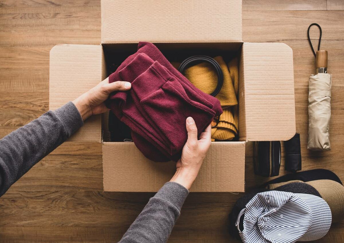 A person carefully puts a maroon shirt into a cardboard box.