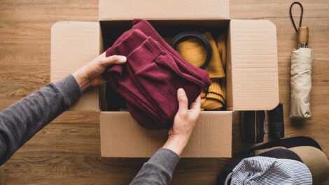 A person carefully puts a maroon shirt into a cardboard box.